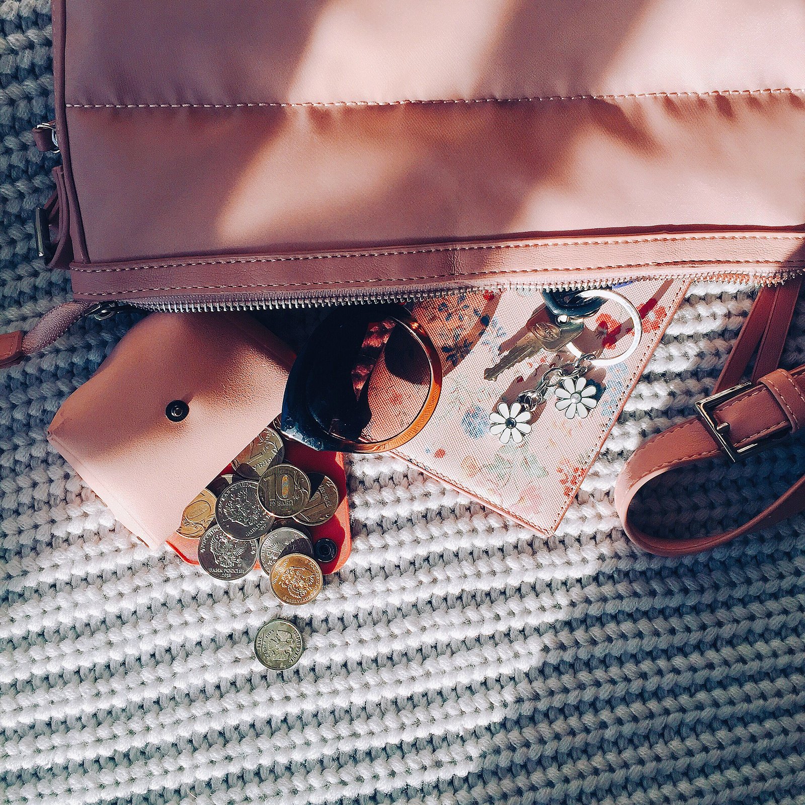 Overhead stylish pink bag with scattered coins from purse and sunglasses with keys on knitwear